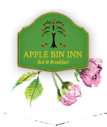 A green sign with a black tree and red apples reads “APPLE BIN INN Bed & Breakfast,” with pink flowers and green leaves illustrated below.
